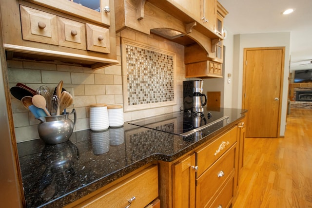 196 Mary Cir, North Mankato, MN 56003 - kitchen with black electric cooktop, brown cabinetry, light wood-style flooring, tasteful backsplash, and dark stone counters