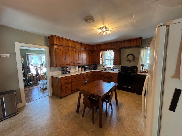 2428 14th Ave E, North Saint Paul, MN 55109 - kitchen featuring black range with electric stovetop, brown cabinets, light countertops, freestanding refrigerator, and light flooring