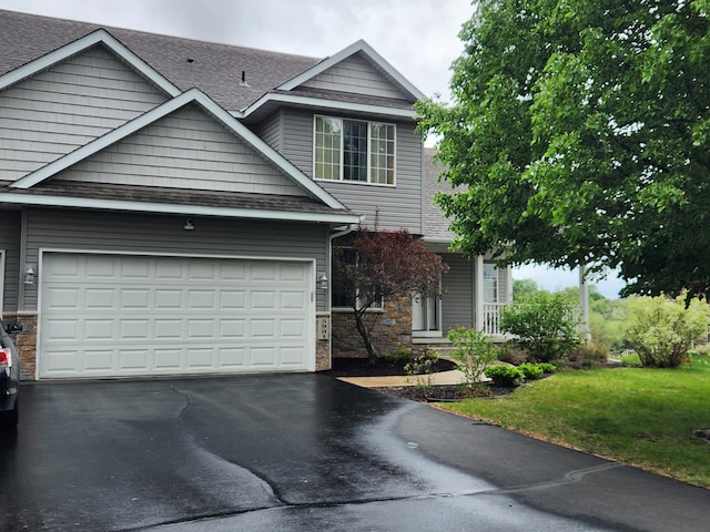 view of front of property featuring stone siding, driveway, roof with shingles, and a front lawn