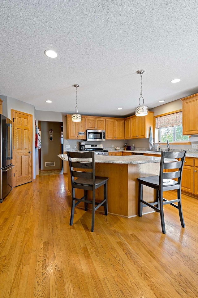 5901 106th Ave N, Brooklyn Park, MN 55443 - kitchen with stainless steel appliances, a textured ceiling, a kitchen bar, brown cabinets, and light wood-style floors