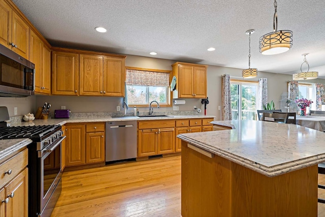 5901 106th Ave N, Brooklyn Park, MN 55443 - kitchen featuring appliances with stainless steel finishes, a center island, a textured ceiling, brown cabinetry, and light wood-style floors