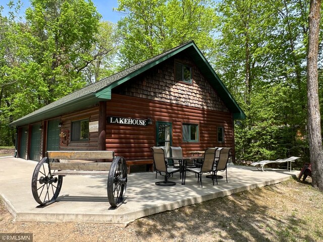 rear view of property with faux log siding, a patio area, and outdoor dining area