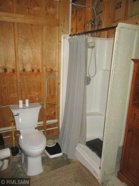 full bathroom featuring a shower stall, toilet, and wood walls