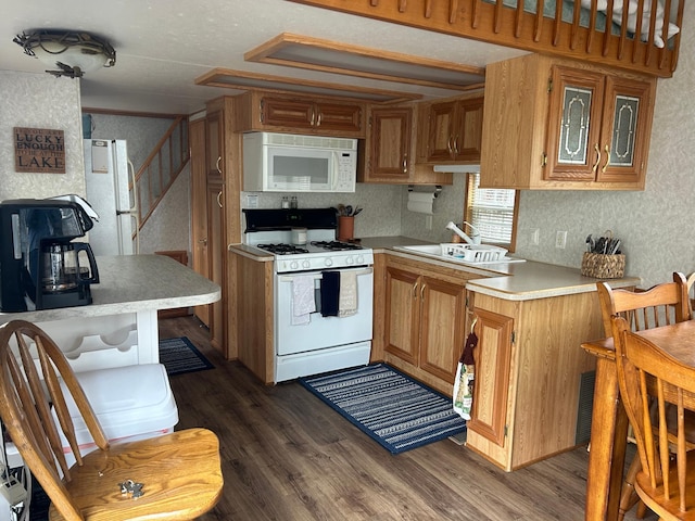 kitchen with white appliances, a sink, light countertops, dark wood finished floors, and wallpapered walls