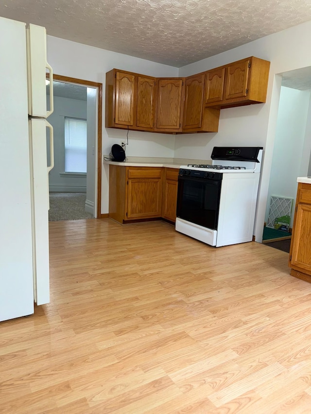 441 Minnesota Ave, Big Lake, MN 55309 - kitchen featuring gas range, freestanding refrigerator, light wood-style flooring, a textured ceiling, and brown cabinets