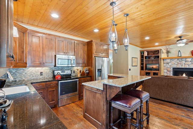 kitchen with appliances with stainless steel finishes, a sink, a kitchen island, dark wood-style floors, and open floor plan