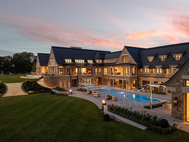 2770 Gale Rd, Woodland, MN 55391 - back of house at dusk with a balcony, a yard, a patio area, an outdoor pool, and stone siding