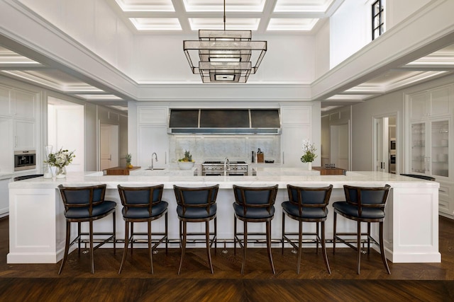 2770 Gale Rd, Woodland, MN 55391 - kitchen featuring custom range hood, coffered ceiling, white cabinetry, a large island with sink, and a breakfast bar