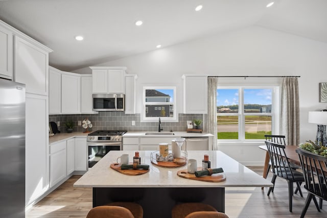 7869 41st St N, Oakdale, MN 55128 - kitchen with stainless steel appliances, lofted ceiling, a breakfast bar area, backsplash, and white cabinets