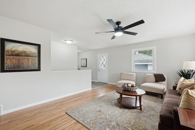 living area with wood finished floors, ceiling fan, baseboards, and a textured ceiling