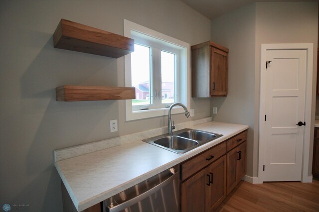 kitchen with a sink, dishwasher, light wood-type flooring, brown cabinetry, and light countertops