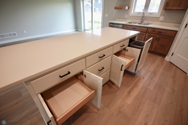 kitchen with a sink, light wood-type flooring, stainless steel dishwasher, light countertops, and brown cabinetry