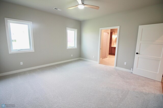 unfurnished bedroom with light carpet, baseboards, ensuite bath, and a ceiling fan