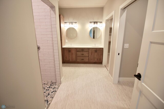 full bath with tiled shower, double vanity, and baseboards