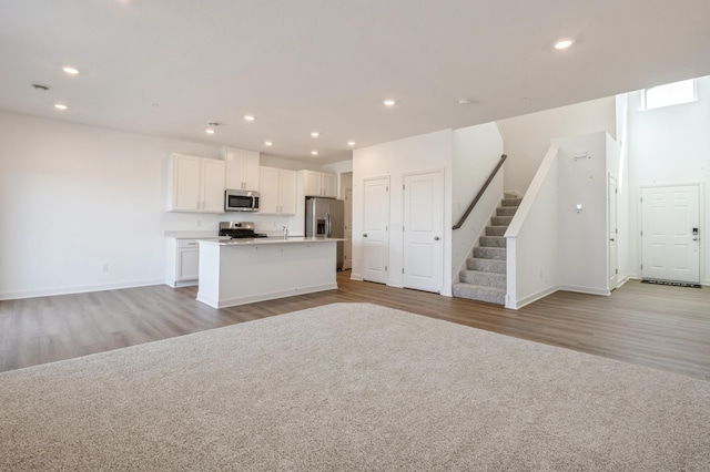 kitchen featuring appliances with stainless steel finishes, light wood-type flooring, open floor plan, a center island with sink, and white cabinetry