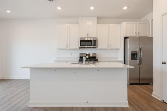 kitchen featuring appliances with stainless steel finishes, a center island with sink, light countertops, wood finished floors, and recessed lighting