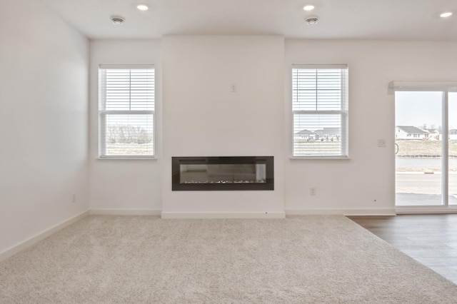 unfurnished living room with healthy amount of natural light, a glass covered fireplace, baseboards, and recessed lighting