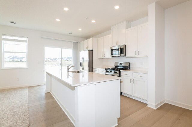 kitchen with stainless steel appliances, a sink, a center island with sink, recessed lighting, and light wood-type flooring