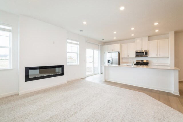 kitchen with stainless steel appliances, a glass covered fireplace, white cabinets, recessed lighting, and baseboards