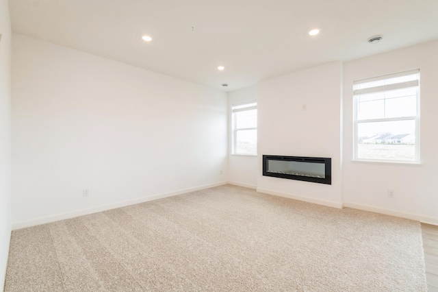 unfurnished living room featuring recessed lighting, a glass covered fireplace, baseboards, and light colored carpet
