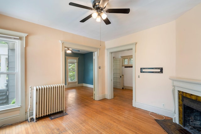 709 7th St SE, Minneapolis, MN 55414 - unfurnished living room featuring radiator heating unit, a ceiling fan, light wood-style floors, a tile fireplace, and baseboards