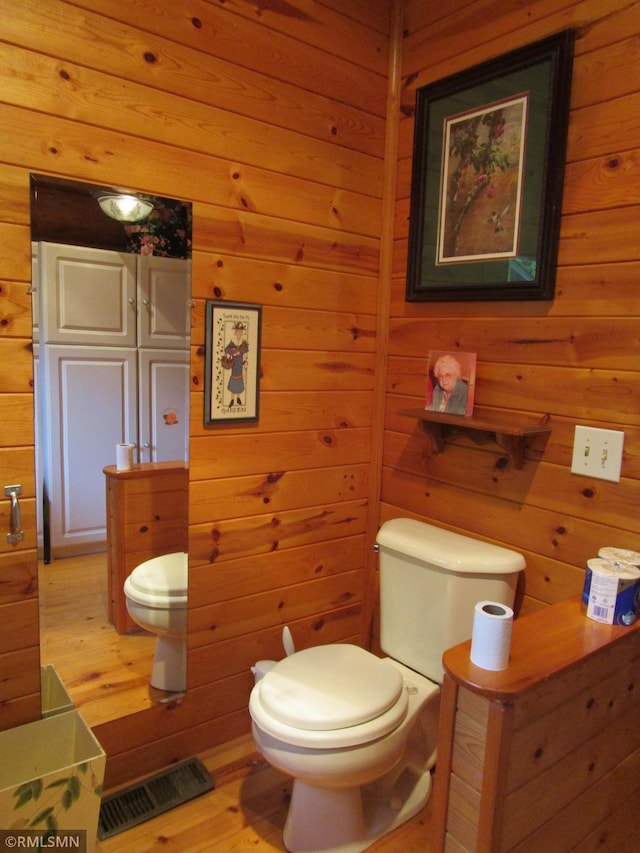 bathroom with toilet, wood walls, and wood finished floors