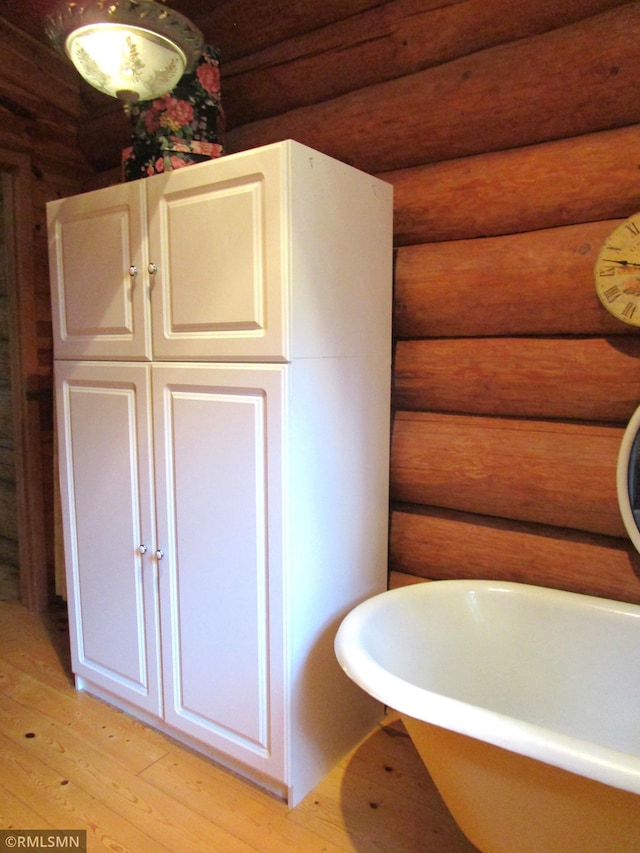 bathroom featuring log walls, wood finished floors, and a freestanding tub