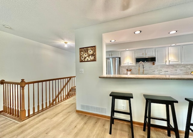 kitchen with appliances with stainless steel finishes, light wood finished floors, a kitchen breakfast bar, tasteful backsplash, and a textured ceiling