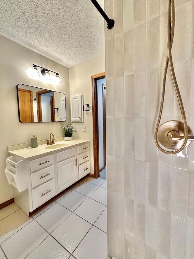 full bath with a tile shower, vanity, a textured ceiling, and tile patterned flooring