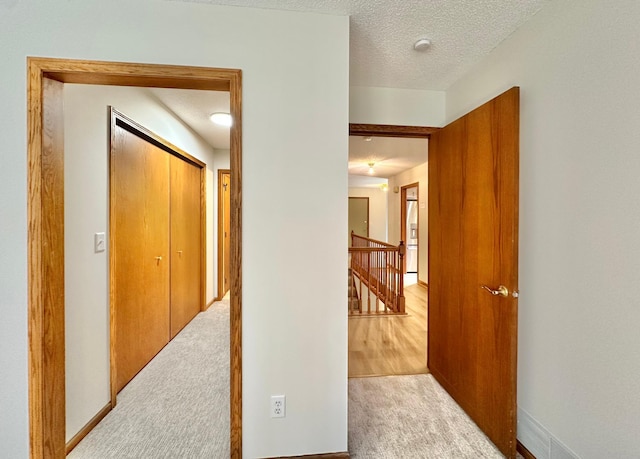 corridor with an upstairs landing, carpet flooring, a textured ceiling, and baseboards