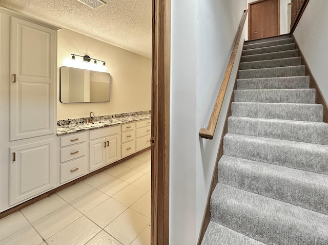 stairway with a textured ceiling and tile patterned flooring