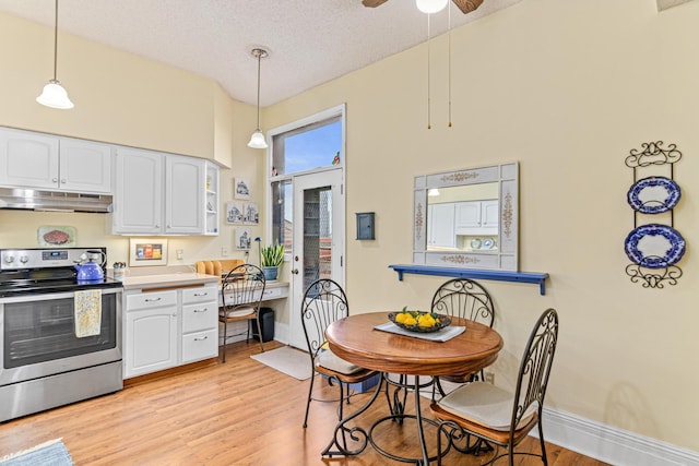 kitchen with stainless steel electric range, under cabinet range hood, light wood finished floors, white cabinets, and a high ceiling