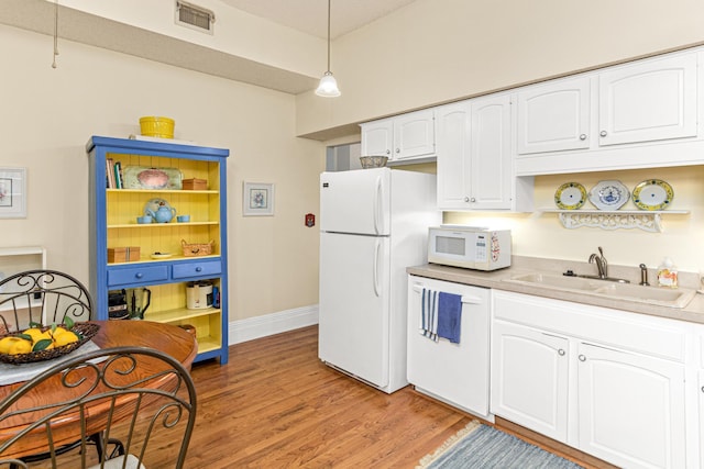 kitchen with a sink, white appliances, white cabinetry, light wood finished floors, and light countertops