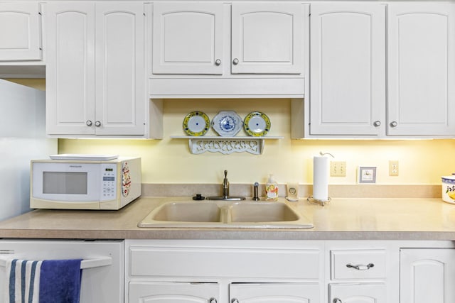 kitchen with white microwave, dishwashing machine, a sink, white cabinetry, and light countertops