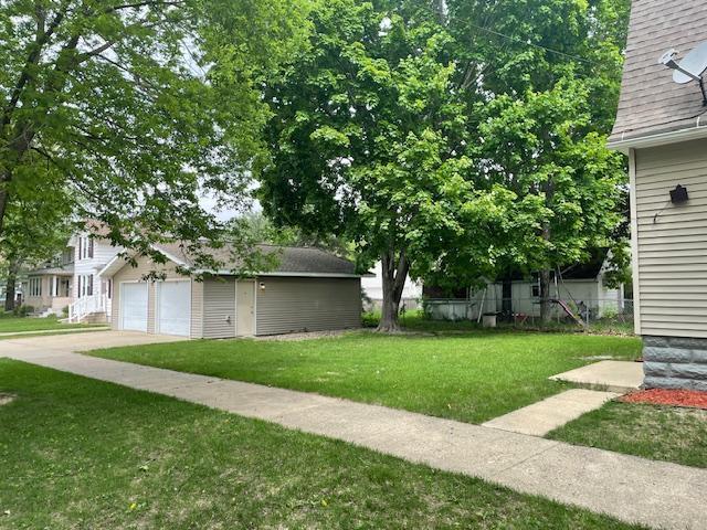 view of green lawn featuring an outdoor structure, a garage, and driveway