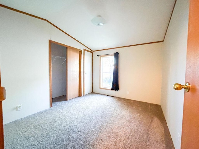 unfurnished bedroom featuring carpet floors, ornamental molding, vaulted ceiling, and a closet