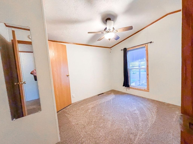 carpeted spare room with lofted ceiling, a ceiling fan, ornamental molding, and a textured ceiling