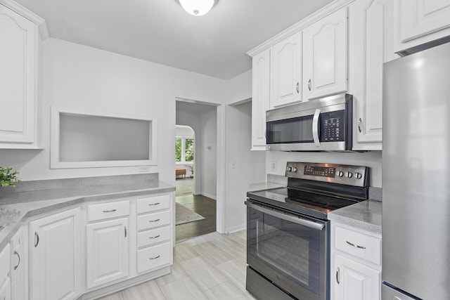 kitchen with appliances with stainless steel finishes, arched walkways, white cabinets, and light countertops