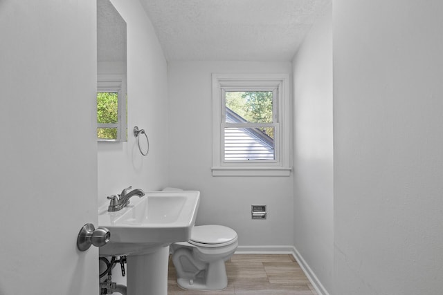 half bathroom featuring toilet, a textured ceiling, and baseboards