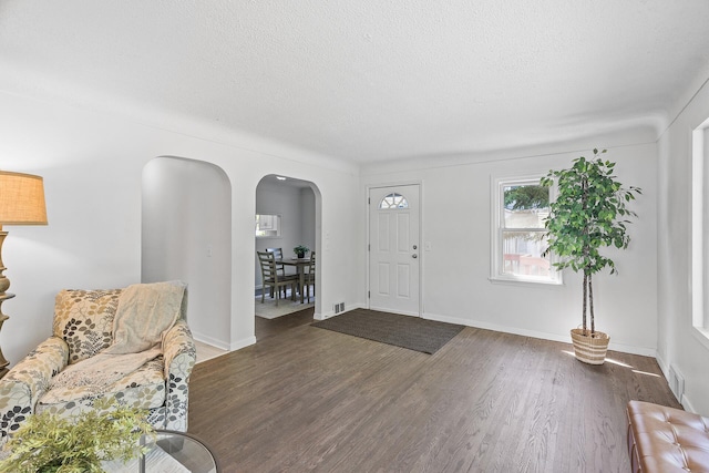 foyer entrance featuring arched walkways, wood finished floors, a textured ceiling, and baseboards