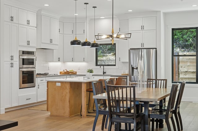 kitchen featuring appliances with stainless steel finishes, light wood-style flooring, a sink, a center island, and backsplash