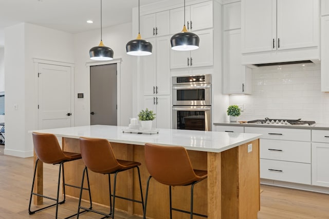 kitchen featuring appliances with stainless steel finishes, a kitchen island, backsplash, light wood-style flooring, and light countertops