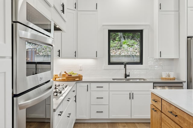 kitchen with a sink, appliances with stainless steel finishes, backsplash, white cabinetry, and light wood-style floors