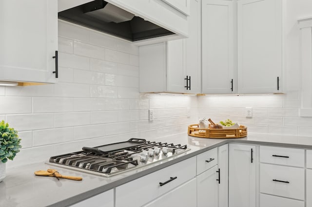 kitchen featuring stainless steel gas cooktop, premium range hood, white cabinetry, and decorative backsplash