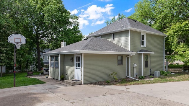 212 4, Montevideo, MN 56265 - rear view of property featuring central air condition unit, roof with shingles, a chimney, a yard, and a patio area