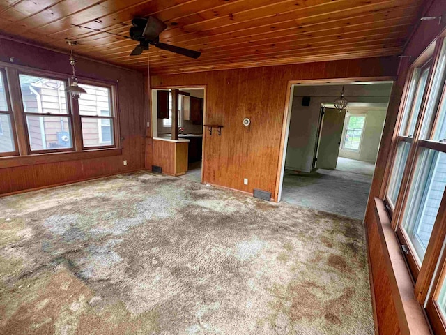 unfurnished living room featuring wood ceiling, carpet, ceiling fan, and wood walls