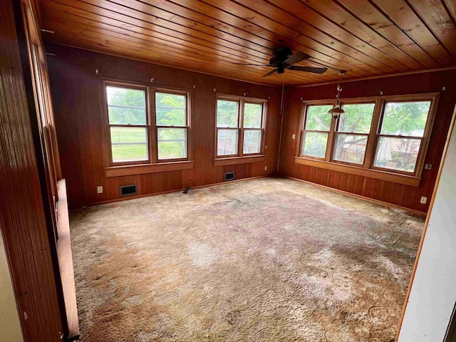 carpeted spare room with wooden ceiling, plenty of natural light, a ceiling fan, and wood walls