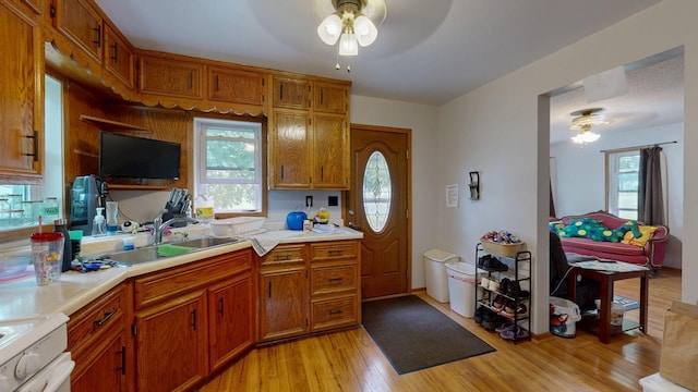 kitchen featuring ceiling fan, brown cabinetry, a sink, stove, and light countertops