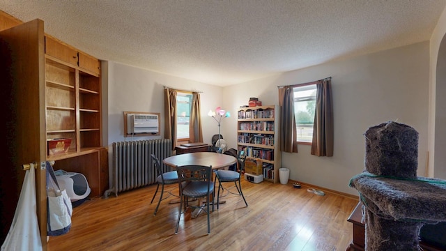 dining room featuring radiator heating unit, light wood-style floors, a textured ceiling, baseboards, and an AC wall unit