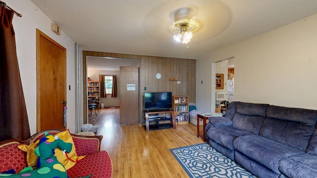 living area featuring light wood-style floors, a ceiling fan, and wood walls